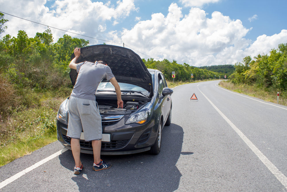 Man looking under the hood of his car that is broke down on the roadway