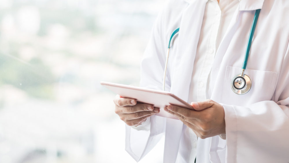 Medical doctor or physician consulting patient's health online using internet mobile digital tablet in clinic or hospital