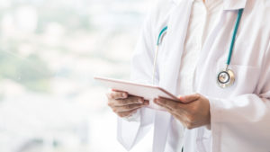 Medical doctor or physician consulting patient's health online using internet mobile digital tablet in clinic or hospital