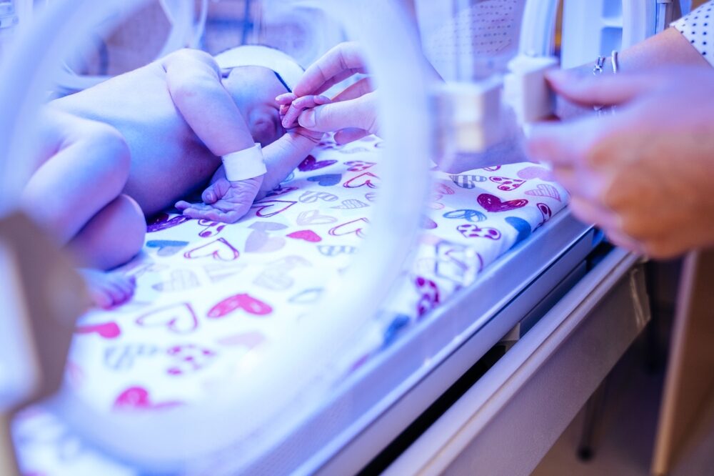 How A Birth Injury Lawyer Can Help Families Protect Injured Children  mother hands caressing and touching her new born baby in intensive care unit in a incubator
