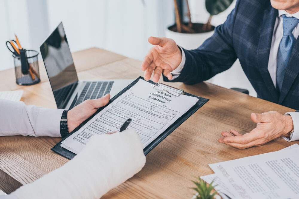 North Carolina Workers’ Compensation: Do I Need An Attorney? cropped view of worker with broken arm signing form for workers compensation claim talking with attorney