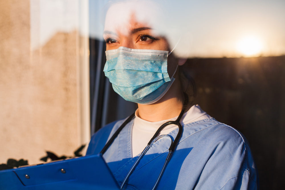 You female caucasian doctor in a mask looking through ICU window