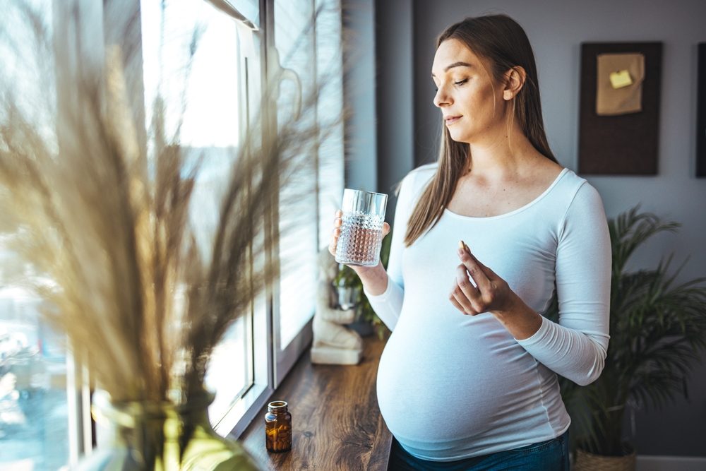 Acetaminophen Use in Pregnancy Linked to ADHD and Autism A young pregnant woman is taking medications and drinking water.