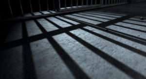 A closeup of view of a jail cells iron bars casting shadows on the prison floor