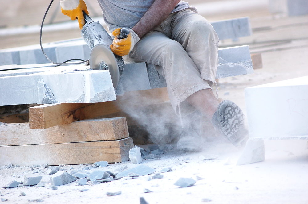 A construction worker using an electric handsaw to cut marble tiles