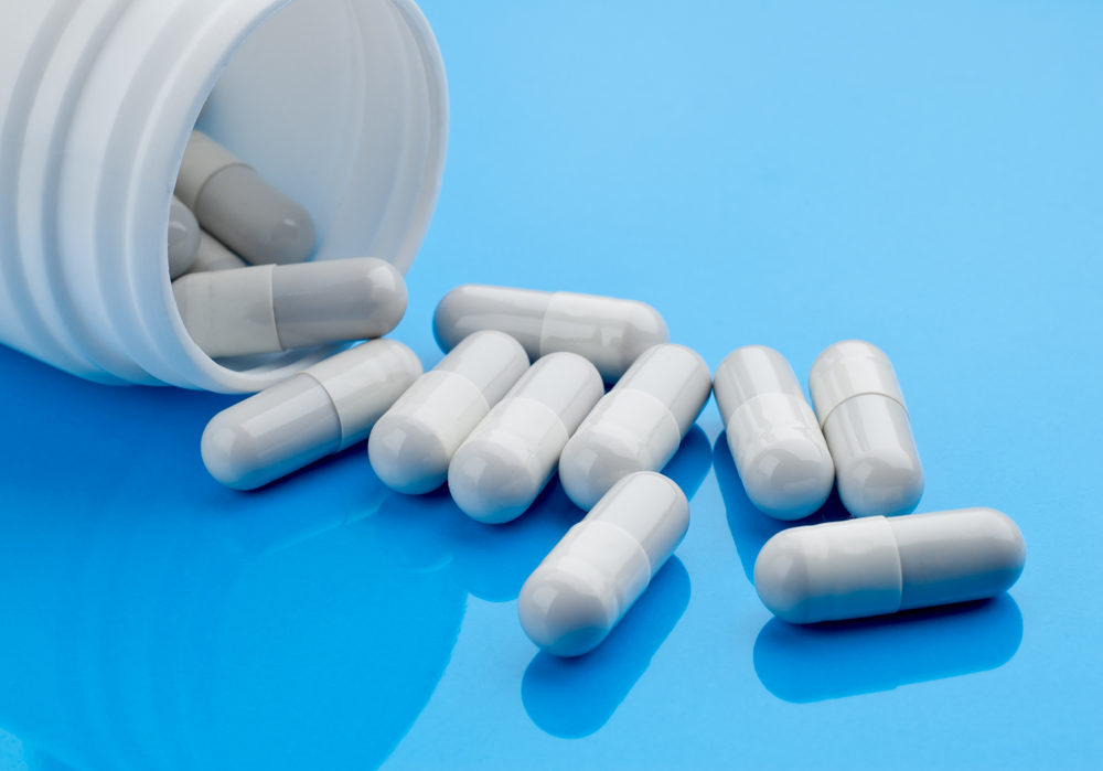 Elmiron and Vision Loss White pill capsules spilling onto a blue table from a bottle