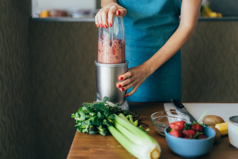 New Jersey Woman Claims SharkNinja Blender Exploded and Caused Serious Injuries woman blending a smoothie at a counter with fruits and vegetables
