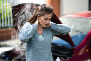 woman holding her neck after car accident with smoke emitting from vehicle
