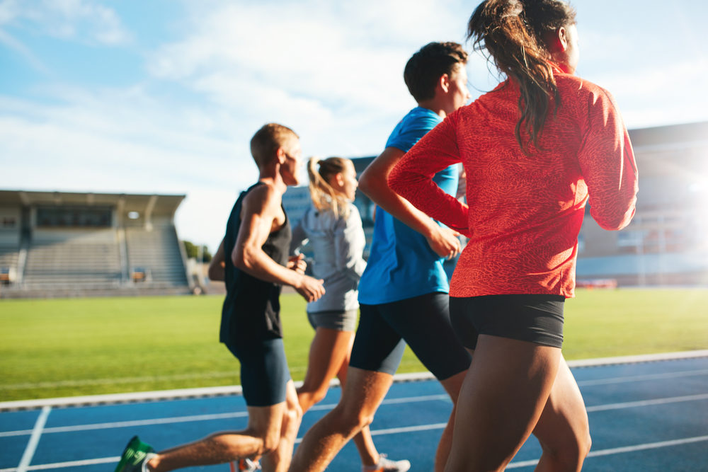 Rear view of young people running together on race track.