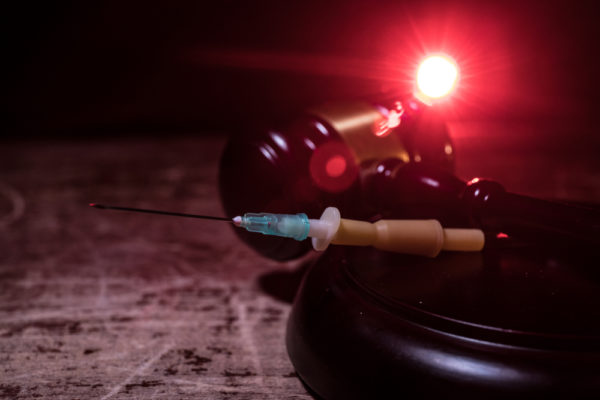lethal injection concept with a syringe and a gavel on a wood desk with a red light behind