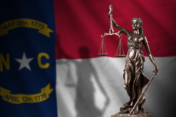 North Carolina US state flag with statue of lady justice and judicial scales in dark room.