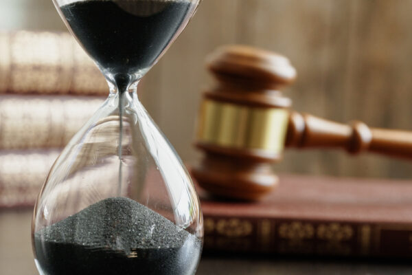 closeup of an hourglass with blurred focus on a gavel and law books in background