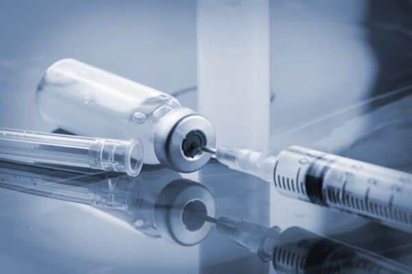 closeup of a glass vial with clear medicine filling a syringe with a dark background